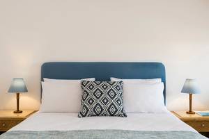 Ein Schlafzimmer im Mitsis Ramira Beach Hotel mit einem Bett, Kissen und Lampen auf den Nachttischen.