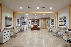 Innenansicht eines Friseursalons mit Stühlen, Spiegeln und Fernsehgeräten.