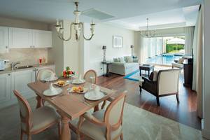 Suite-Esszimmer im Titanic Deluxe Golf Belek mit Esstisch, Früchteteller und Swimmingpool im Hintergrund.
