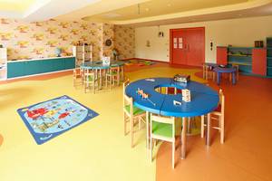 Ein Kinderspielzimmer mit runden Tischen und Sitzen, gelbem Boden und bunten Wandgestaltungen.