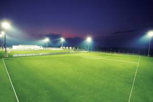 Fussballplatz bei Nacht mit Flutlichtern und leerem Spielfeld