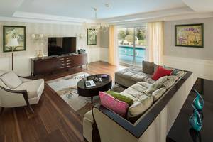 Wohnzimmer im Titanic Deluxe Golf Belek mit großer Couch, Fernseher und Swimmingpool.