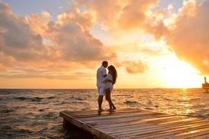 Paar auf Holzsteg bei Sonnenuntergang im Bandos Maldives