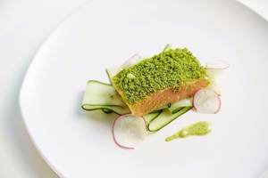 Ein Gericht mit Lachs auf Gurke, umgeben von Radieschen und sauereis.