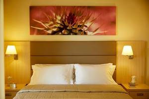 Schlafzimmer im Capo Di Corfu Hotel mit Doppelbett, Nachttischen und Wandkunst.