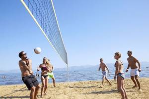 Mehrere Personen spielen Volleyball auf einem Strand am Tag.