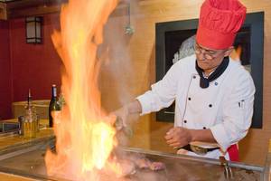 Koch im Restaurant brät Fleisch auf einem Grill mit Flammen.