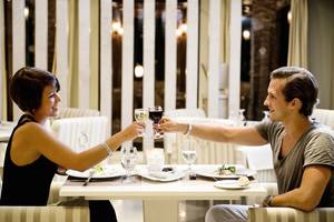 Ein Paar sitzt an einem Tisch im Restaurant und stößt mit Weingläsern an.