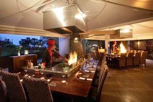 Ein Koch bereitet am Tisch im GrandResort Limassol ein Gericht mit einem Feuergrill zu.