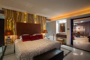 Hotelzimmer im GrandResort Limassol mit luxuriösem Bett, Marmorwand und offenem Eingang.