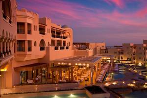 Luftaufnahme des Kempinski Hotels Soma Bay bei Sonnenuntergang mit rosa Himmel und beleuchtetem Poolbereich.