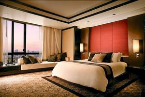 Schlafzimmer im Banyan Tree Bangkok mit großem Bett, Tagesbett, rote Wand und Aussicht.
