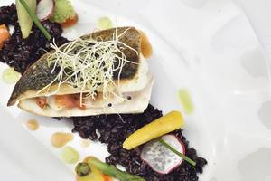 Gegrillter Fisch auf schwarzem Reis und Gemüse auf einem weißen Teller