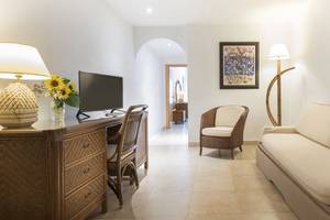 Innenansicht eines Zimmers im Princess Inspire Tenerife Hotel mit Schreibtisch, Sessel, Couch und Kunstwerk.