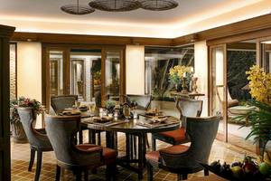 Esszimmer im Rayavadee Hotel mit runden Tisch und Stühlen, Glastüren und gelben Blumen im Vordergrund.