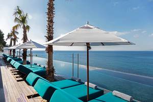 Außenterrasse des Mitsis Summer Palace Beach Hotels mit Liegen und Sonnenschirmen, die zum Meer zeigen.