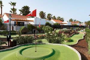 Minigolfkurs vor dem Hotel Barcelo Fuerteventura Castillo mit roten Flaggen und Palmen im Hintergrund.