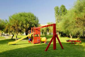 Kinderspielplatz im Platanista Hotel mit gelber Rutsche und roten Schaukeln.