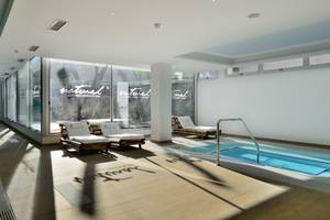 Poolbereich im Alexandre Hotel Troya mit Liegestühlen und großer Fensterfront.