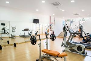 Fitnessraum im Alexandre Hotel Troya mit diversen Trainingsgeräten und Spiegeln.
