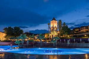 Candia Park Village Hotel Außenbereich mit beleuchtetem Pool und Uhrturm bei Nacht