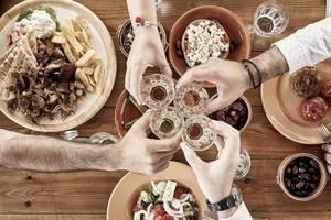 Menschen am Tisch mit griechischem Essen, Salate, Fleisch und Getränke.