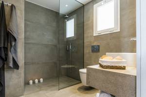 Badezimmer im Candia Park Village Hotel mit grauen Fliesen, Glasdusche und Waschbecken.