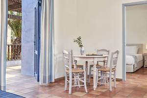 Inneneinrichtung eines Zimmers im Candia Park Village Hotel mit Tisch, Stühlen und einem Blick auf einen Balkon und ein Bett.