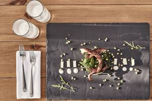 Gegrillter Tintenfisch mit Salat auf einem schwarzen Teller auf einem Holztisch mit zwei Gläsern Wasser, Gabeln und Servietten.