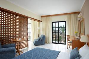 Innenansicht eines Zimmers im Porto Bello Beach Hotel mit Bett, Sofa, Tisch und Terrassentür.