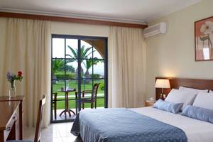 Schlafzimmer im Porto Bello Beach Hotel mit Bett, Tisch und Stuhl vor einer Terrasse
