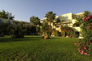 Außenansicht des gelben Porto Bello Beach Hotels mit grüner Rasenfläche und Blumen