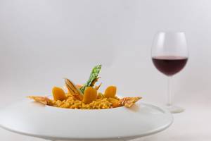 Ein Gericht mit Reis, Garnelen und Gemüse in einer weißen Schüssel, neben einem Glas Rotwein.