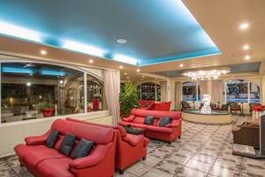 Innenbereich des Kalyves Beach Hotels mit roten Sofas und Tisch, einem Brunnen und einer blauen Decke.