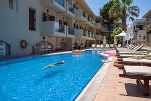 Eine Person schwimmt im Pool des Kalyves Beach Hotels, umgeben von Sonnenliegen und Palmen.
