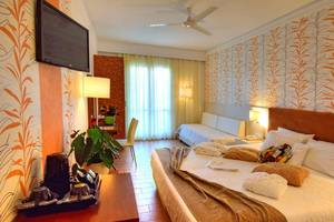Hotelzimmer im Kalyves Beach Hotel mit Fernseher, Deckenventilator, Bett und Sofa.