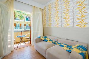 Zimmer im Kalyves Beach Hotel mit Balkon, Sofa, Tisch und Blick auf die Straße.