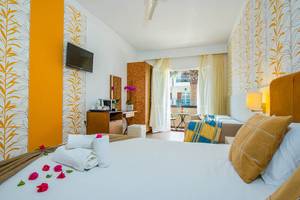 Innenansicht eines Zimmers im Kalyves Beach Hotel mit farbenfrohen Wänden, einem Bett, Fernseher und Balkon.