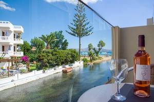 Aussicht von Kalyves Beach Hotel auf Strand und Kanal mit einem Glas und einer Flasche Wein auf dem Tisch.