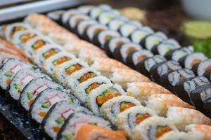 Eine Auswahl an verschiedenen Sushi-Rollen, die auf einem schwarzen Teller serviert werden.