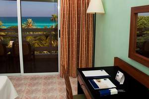 Zimmer im Occidental Arenas Blancas Hotel mit Meerblick, Glastür und Schreibtisch.