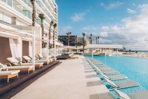 Poolbereich im Coral Level at Iberostar Selection Cancun mit vielen Liegen und einem Blick auf das Meer.