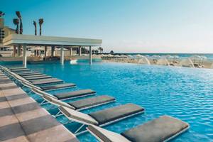 Infinity-Pool am Coral Level at Iberostar Selection Cancun mit Sonnenliegen und Blick auf den Strand.
