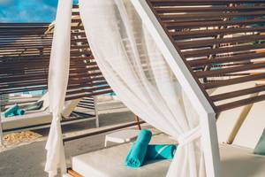 Reihe von Loungebetten am Strand des Coral Level at Iberostar Selection Cancun, bedeckt mit weißen Vorhängen und blauen Handtüchern.