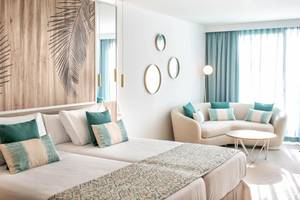 Ein modernes Hotelzimmer im Guayarmina Princess Hotel mit zwei Betten, blauen Kissen und einer gemütlichen Couch.