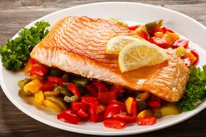 Ein Teller mit gebratenem Lachs, Zitrone und buntem Gemüse.