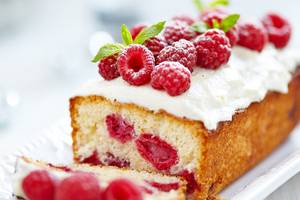 Ein Kuchen mit Himbeeren und weißer Creme auf einem weißen Teller.