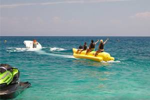 Mehrere Personen auf einem gelben Wassersport-Boot im Meer, gezogen von einem grünen Jetski.