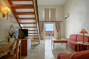Innenansicht des Wohnzimmers im Mitsis Family Village Beach Hotel mit Sofa, Tisch, Fernseher und Balkon