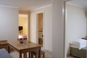Innenansicht eines Zimmers im Mitsis Family Village Beach Hotel mit Tisch, Obstschale und Schlafzimmer.